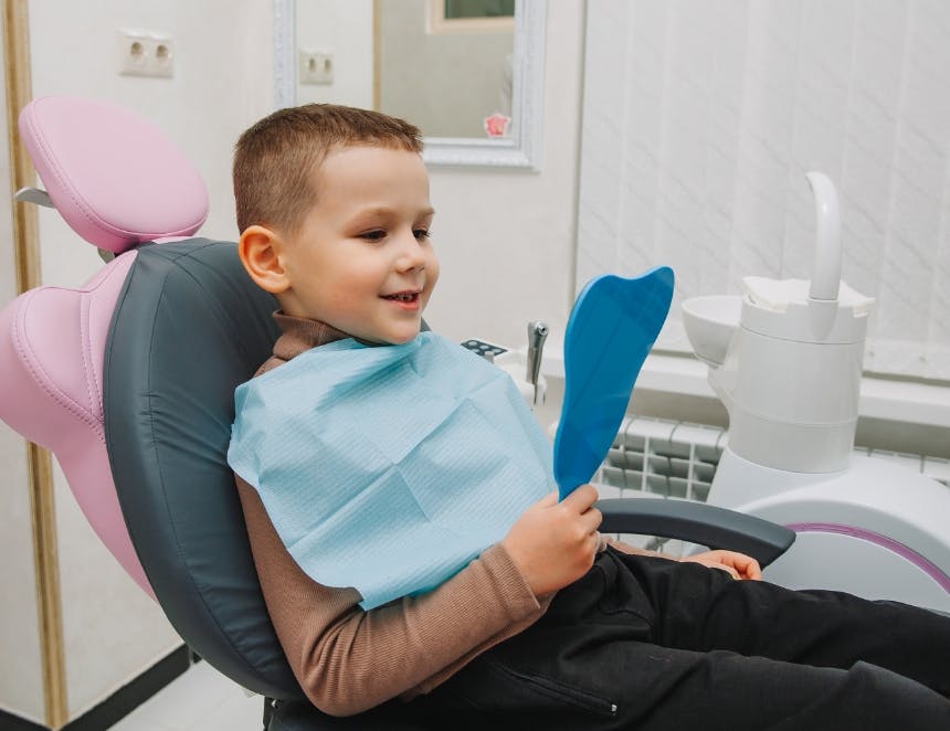 boy-looks-mirror-with-toothy-smile-sitting-chair-with-dentist-dental-office